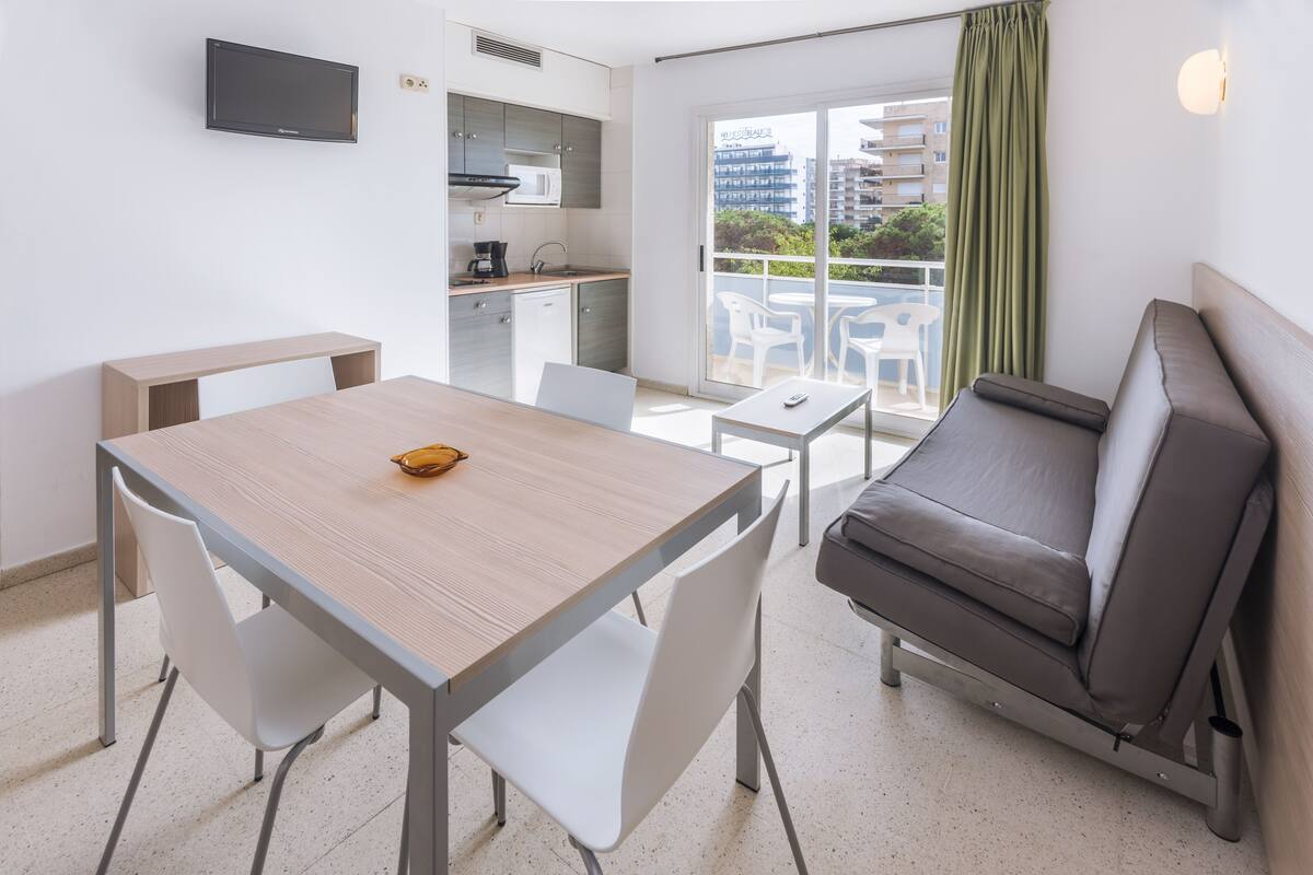 Un espace de vie compact comprenant une kitchenette, un coin repas, un canapé et un balcon offrant une vue sur la ville.
