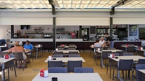 Een terras met tafels en stoelen, een bar met flessen op de planken, en een toonbank waar personeel eten serveert.
