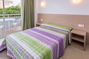 Une chambre d’hôtel avec un grand lit, une tête de lit en bois, une table de chevet et une vue sur la verdure et les bâtiments environnants.