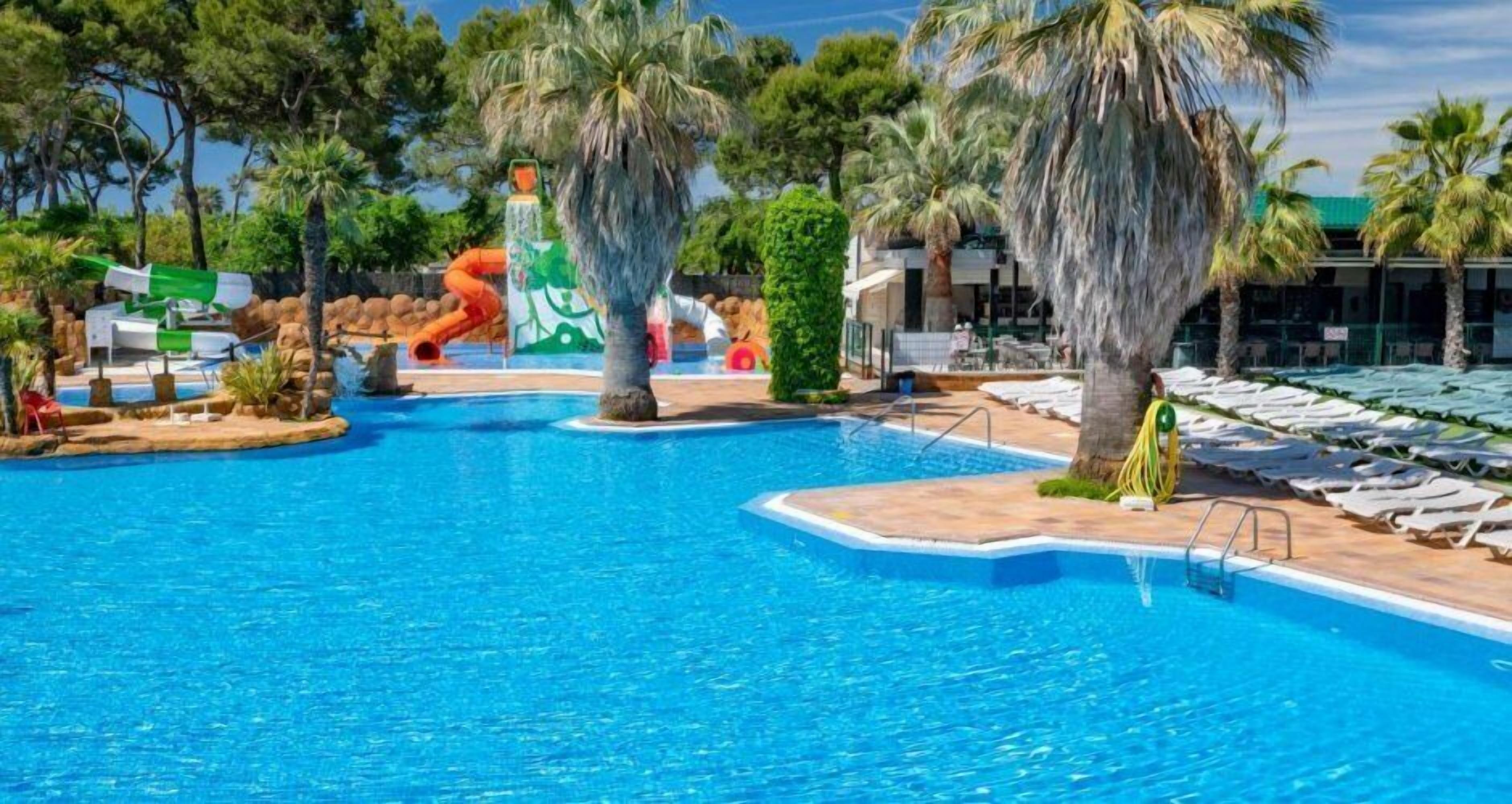 Una piscina con tobogán, palmeras y sillas de descanso.