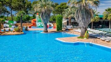 Una piscina con tobogán, palmeras y sillas de descanso.