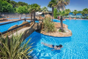 Une piscine avec un îlot rocheux et des palmiers.