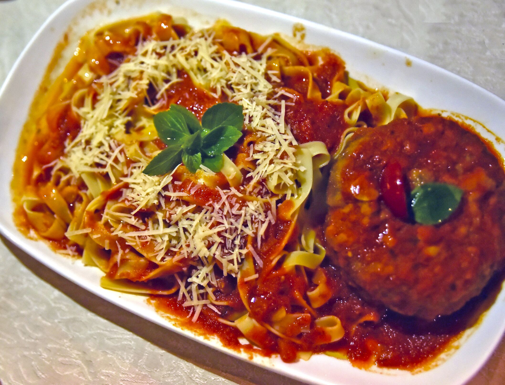 A plate of pasta with meatballs and grated cheese, garnished with a basil leaf.