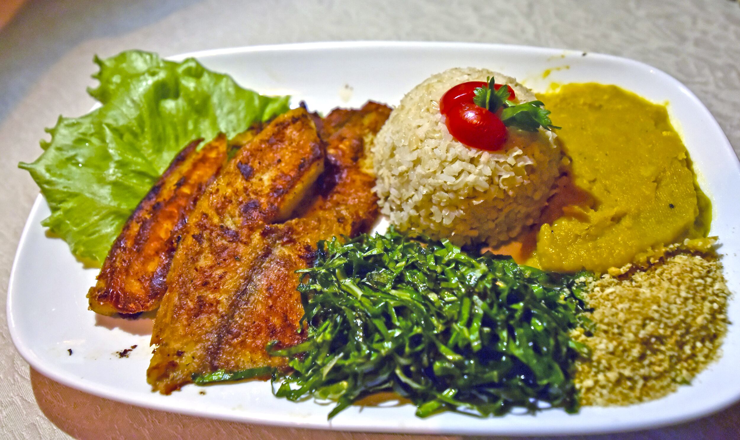 A plate with grilled chicken, rice, a side of greens, and a yellow sauce.