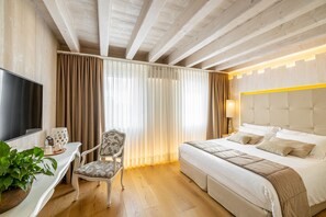 Ett hotellrum med en säng, ett skrivbord med en tv, en stol och ett stort fönster med gardiner.