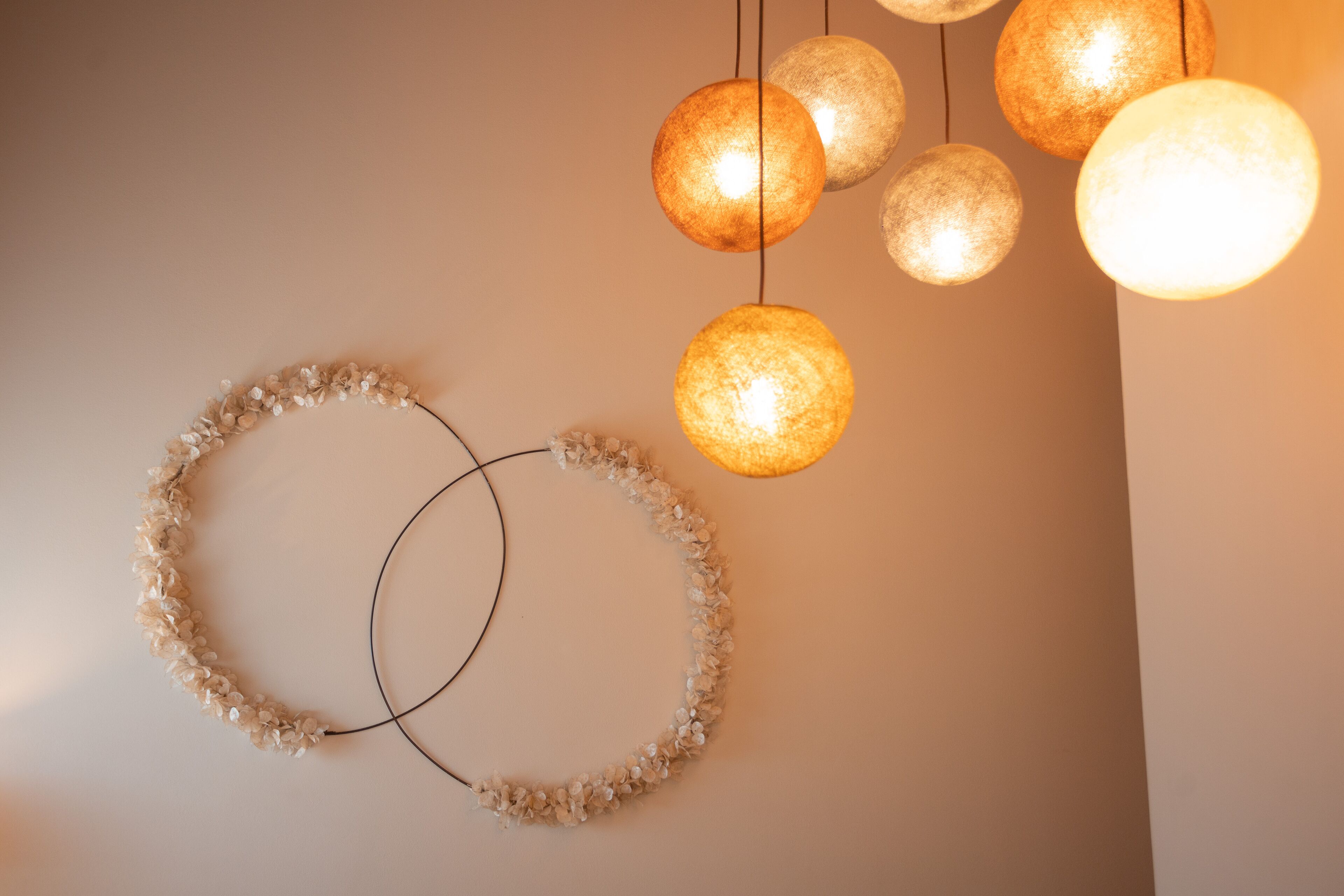 Una pared con un arreglo floral circular y varias lámparas esféricas.