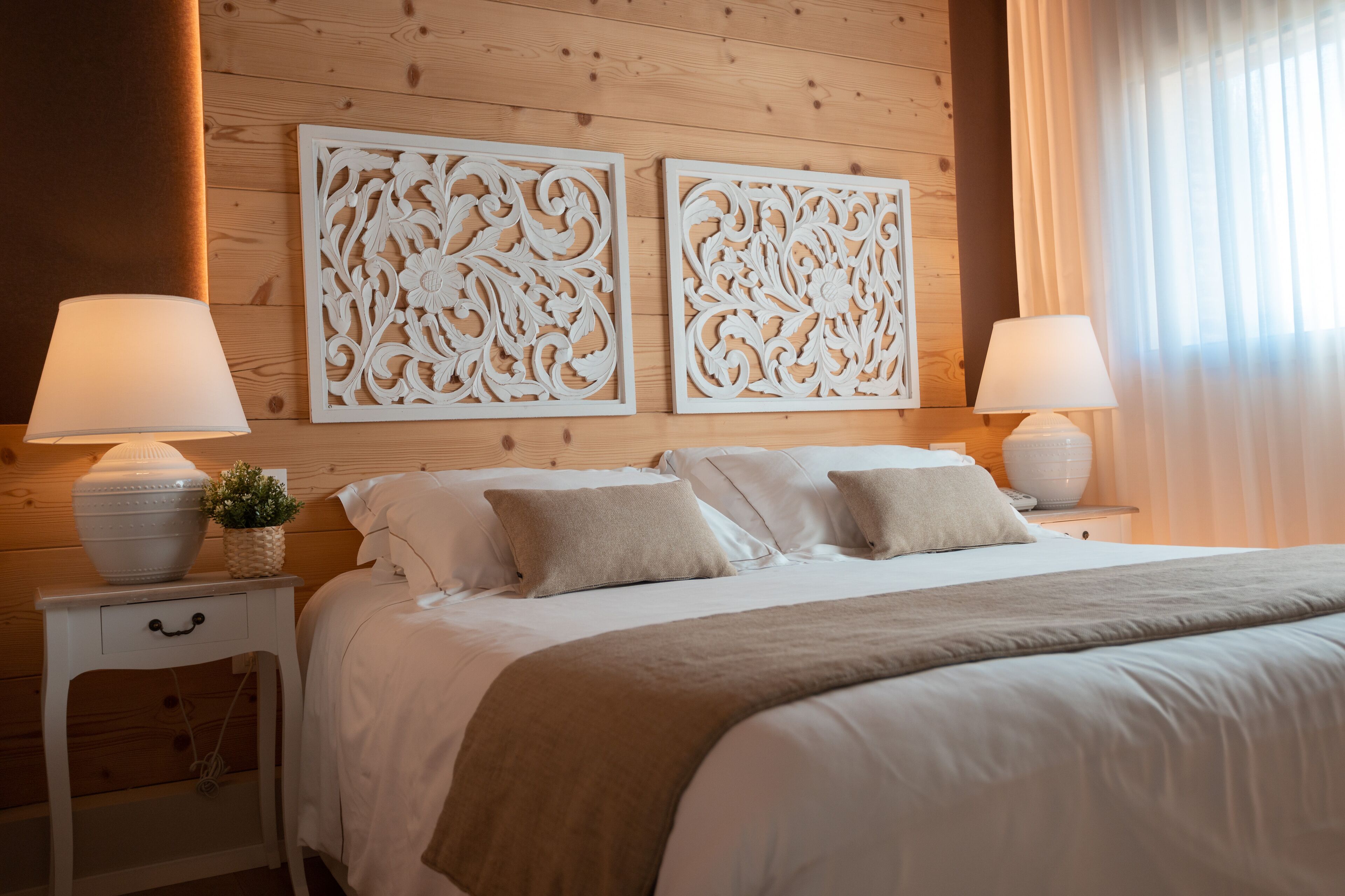 Una cama bien hecha con una manta color beige, dos mesitas de noche con lámparas y decoración en la pared.