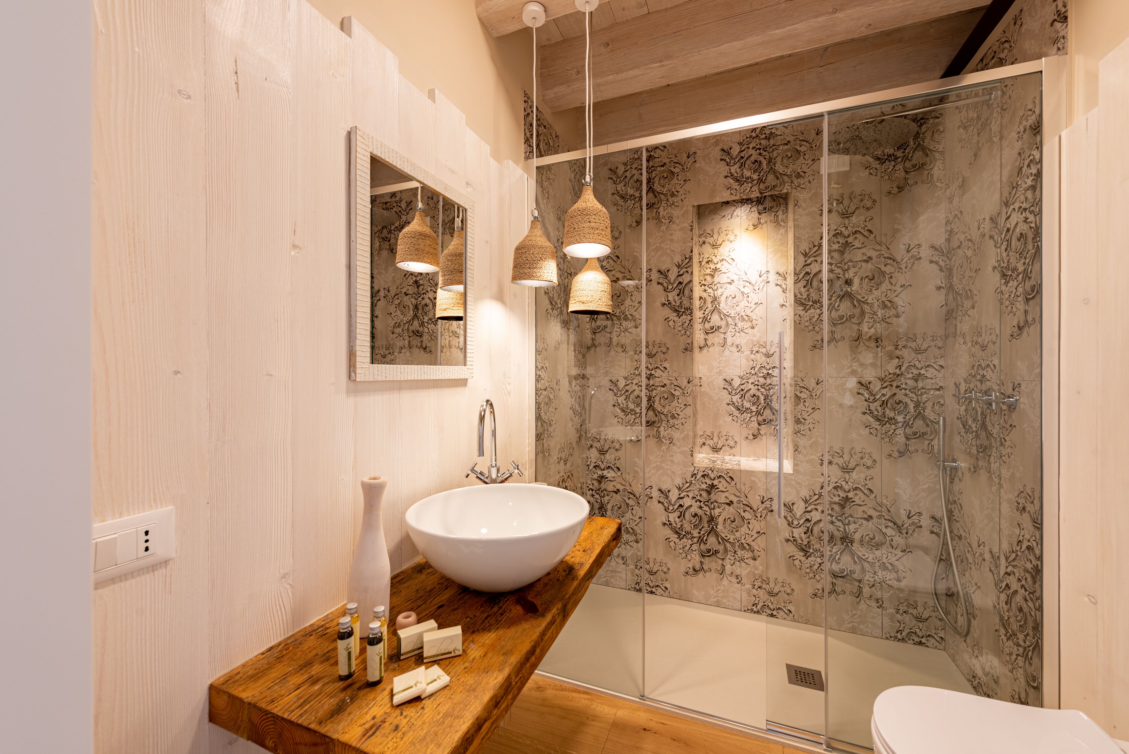 Ein modernes Badezimmer mit einem hölzernen Waschtisch, einem großen weißen Waschbecken und einer Duschkabine mit Glas und dekorativen Fliesen.