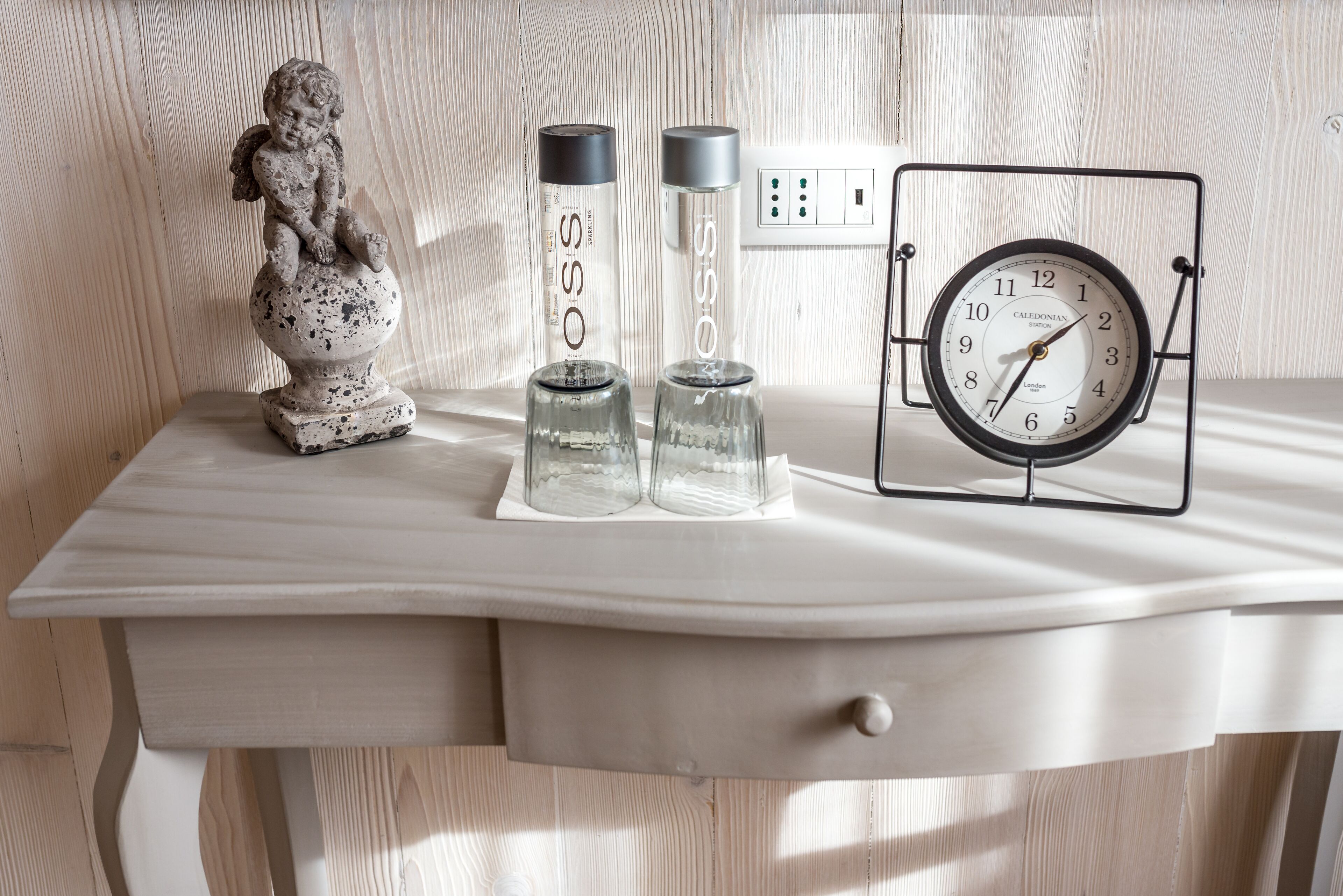 Ein weißer Schreibtisch mit einer Uhr, zwei Wasserflaschen und einer Statue.