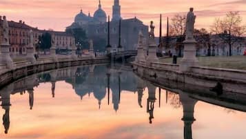 Un cuerpo de agua tranquila que refleja un edificio histórico y estatuas, bajo un cielo despejado.