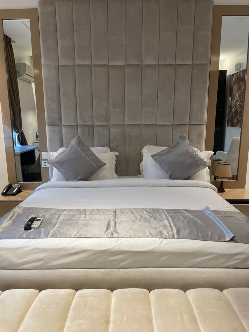 A hotel room with a large bed, a headboard with a padded design, two bedside tables with lamps, and a telephone on the left side of the bed.