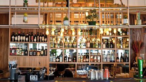 Un bar avec des étagères remplies de bouteilles d’alcool, un barman qui travaille et des lampes suspendues.