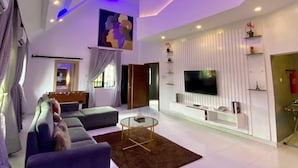 A modern living room with a sofa set, a TV mounted on the wall, and a ceiling with blue lighting. - Proof Lounge Hotel (Lagos)