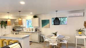 A modern kitchen with white cabinets, a central island, and pendant lighting. There is a dining area with a round table and chairs. - South Oceanside 1br/1bath, clean and beach close (Oceanside)