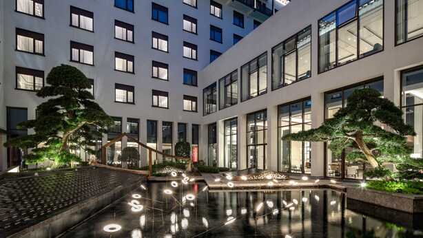 A modern hotel with a courtyard featuring a reflective pool, potted trees, and a seating area. - Crowne Plaza Wuzhen by IHG (Jiaxing)