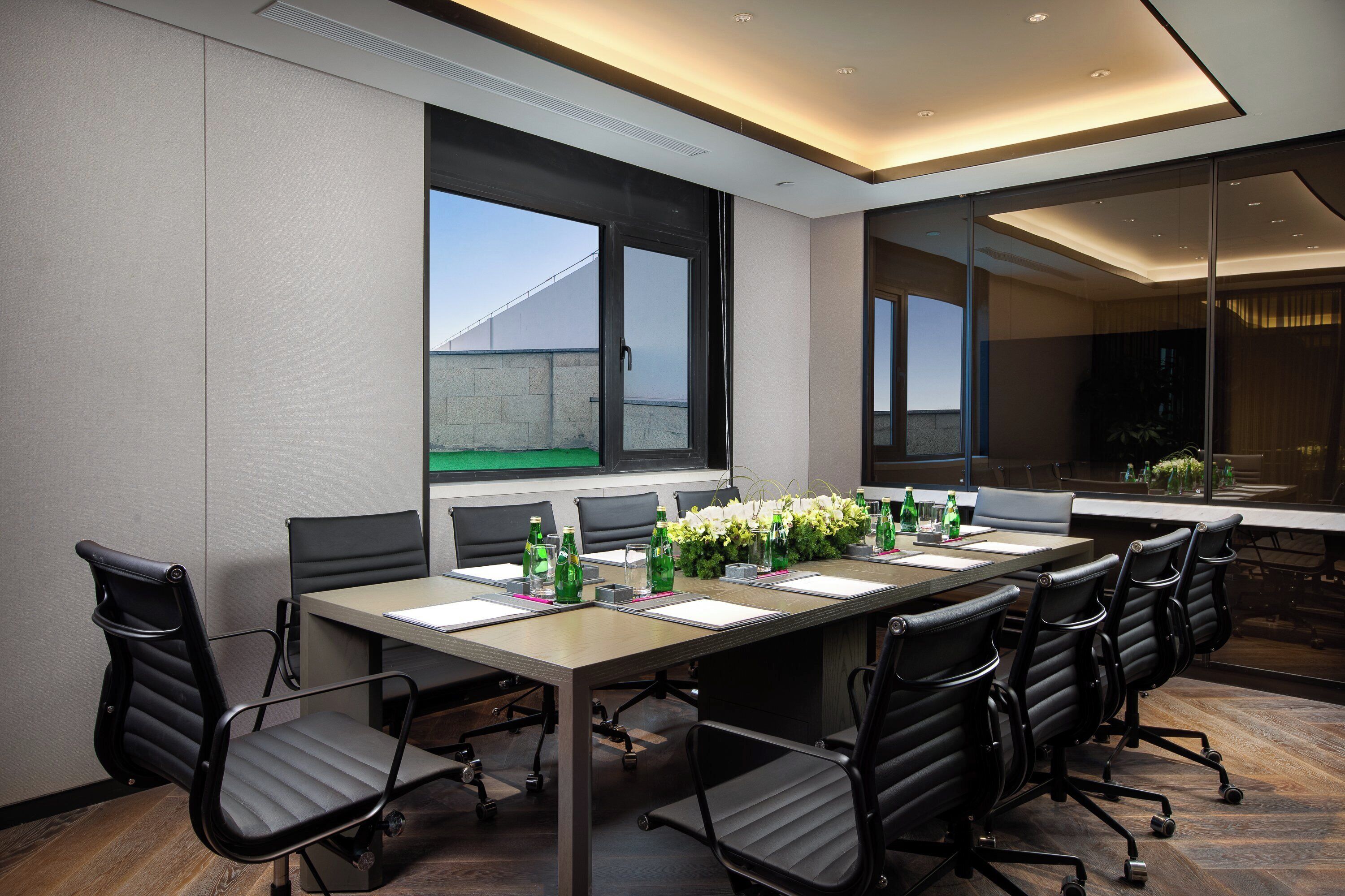 A conference room with a long table, black chairs, and a window with a view of a building.