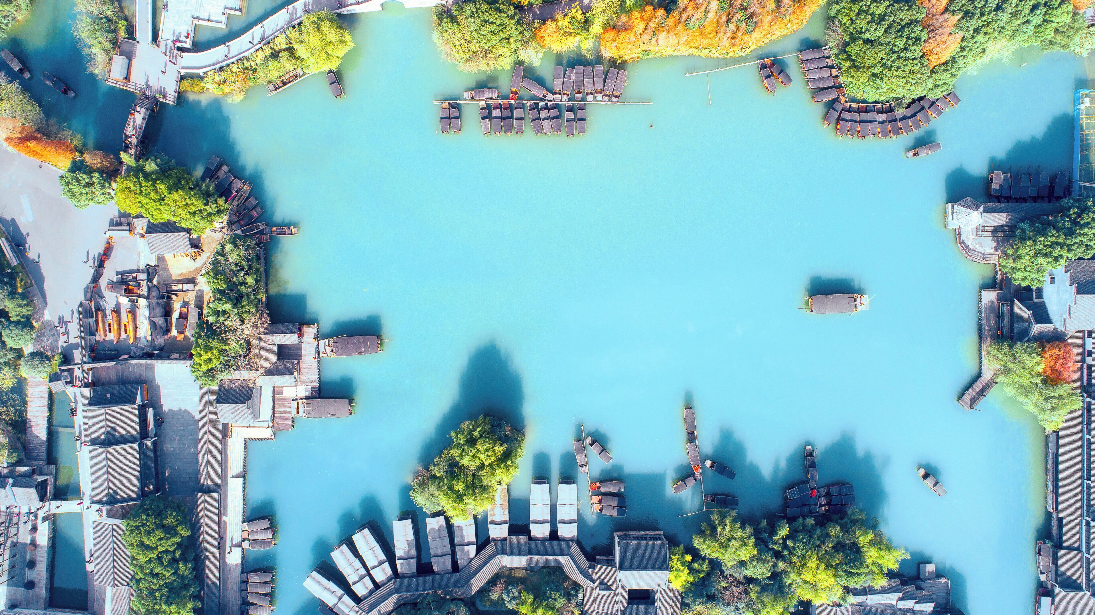 An aerial view of a waterfront property with docked boats, a docked yacht, and a building with a sloped roof.