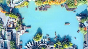 An aerial view of a waterfront property with docked boats, a docked yacht, and a building with a sloped roof. - Crowne Plaza Wuzhen by IHG (Jiaxing)