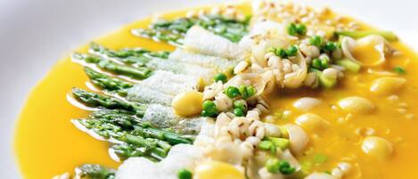 Un plato blanco con un guiso de pescado, espárragos, guisantes y judías en salsa amarilla.