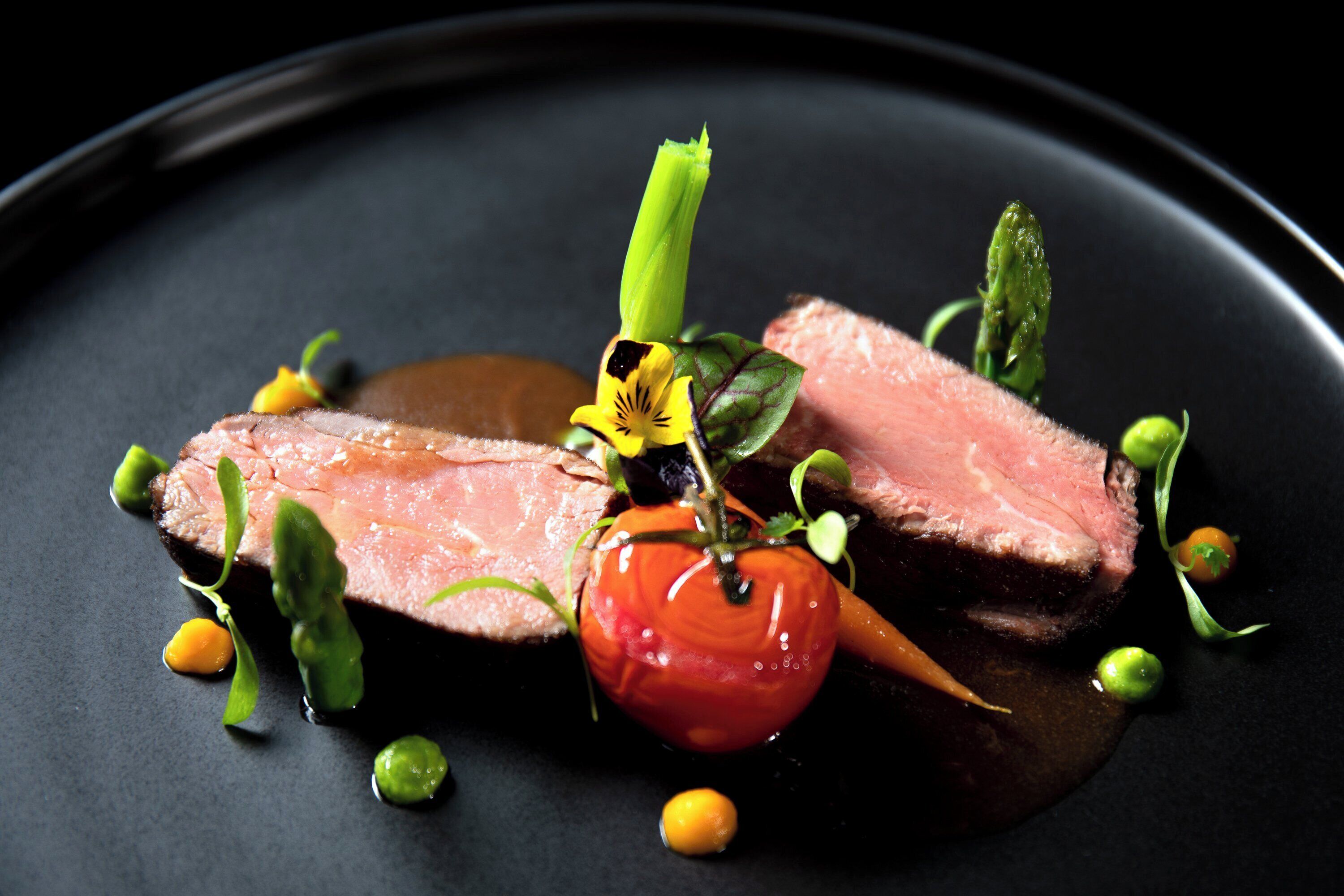 A plate of food with slices of meat, vegetables, and a decorative flower.