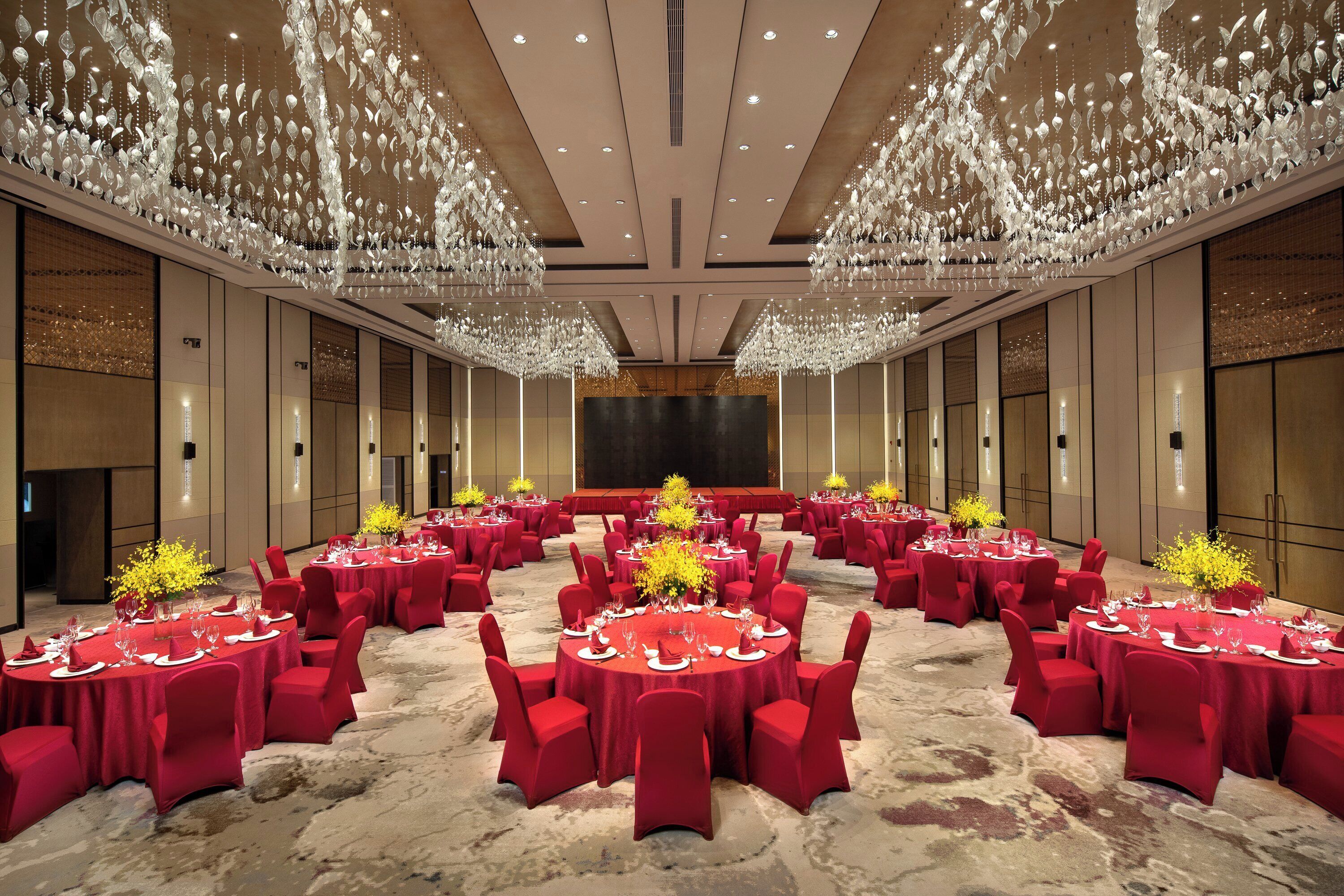 A banquet hall with round tables, red chairs, and a large stage.
