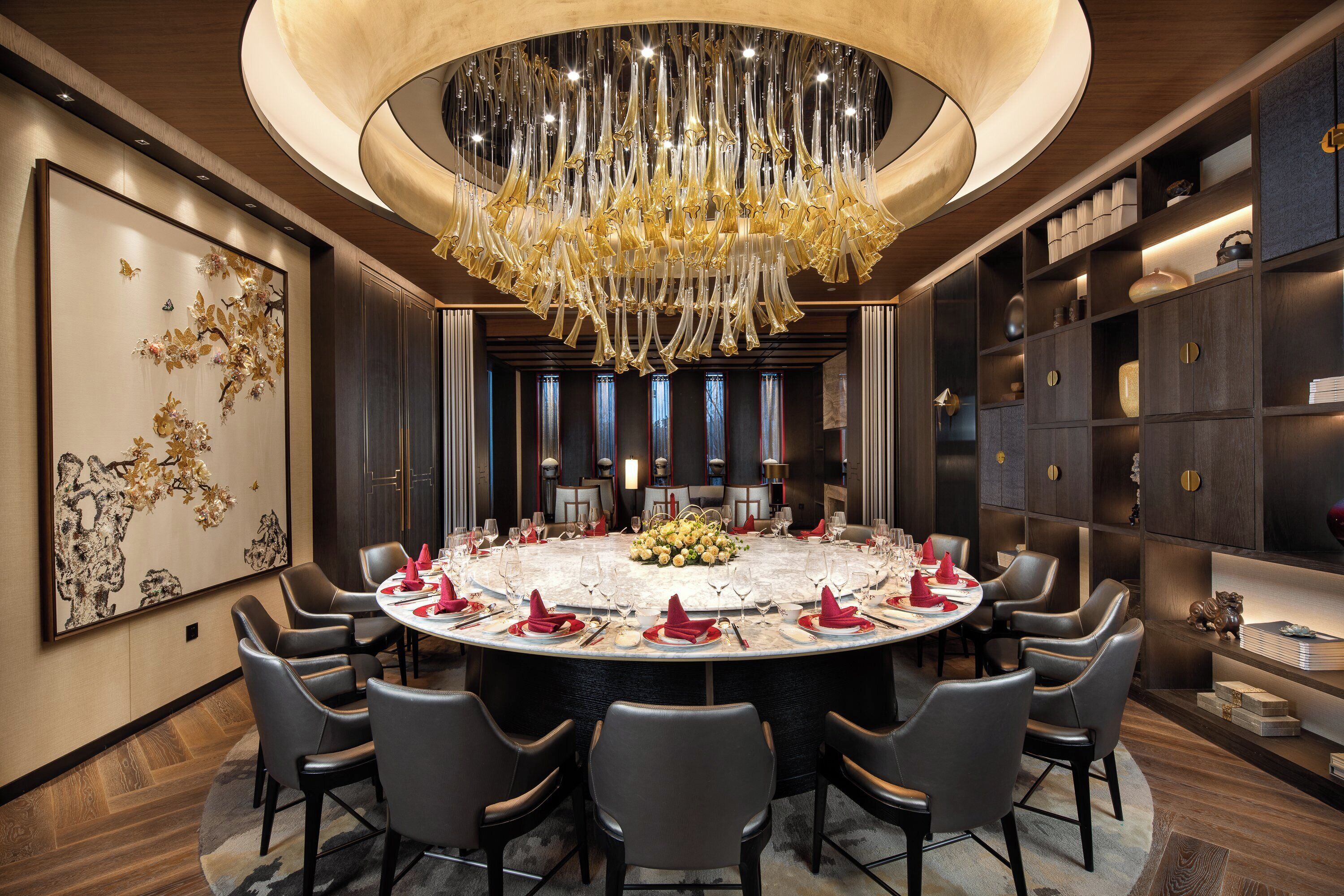 A round dining table with chairs, a chandelier, and a decorative wall piece.