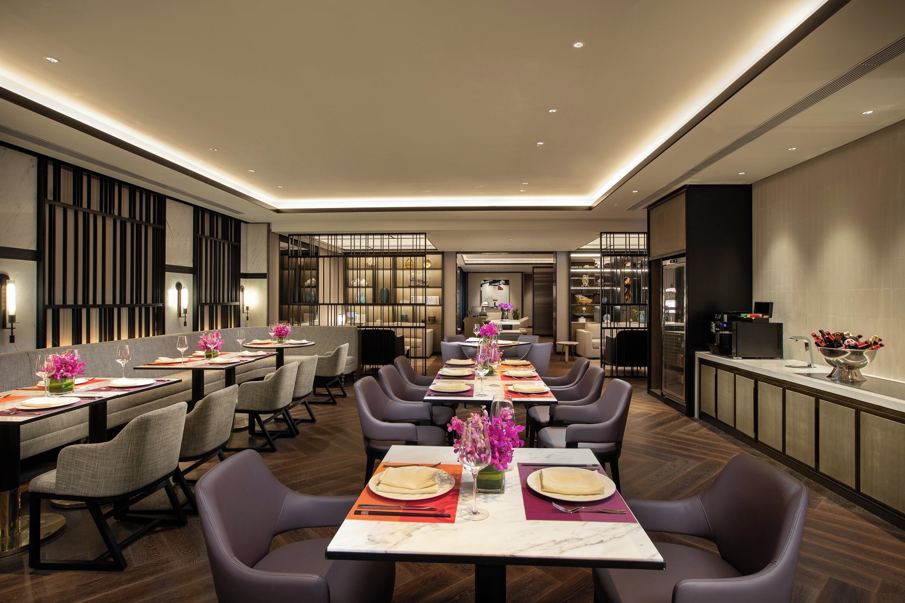 A modern dining area with multiple tables, chairs, and a kitchen area visible in the background.