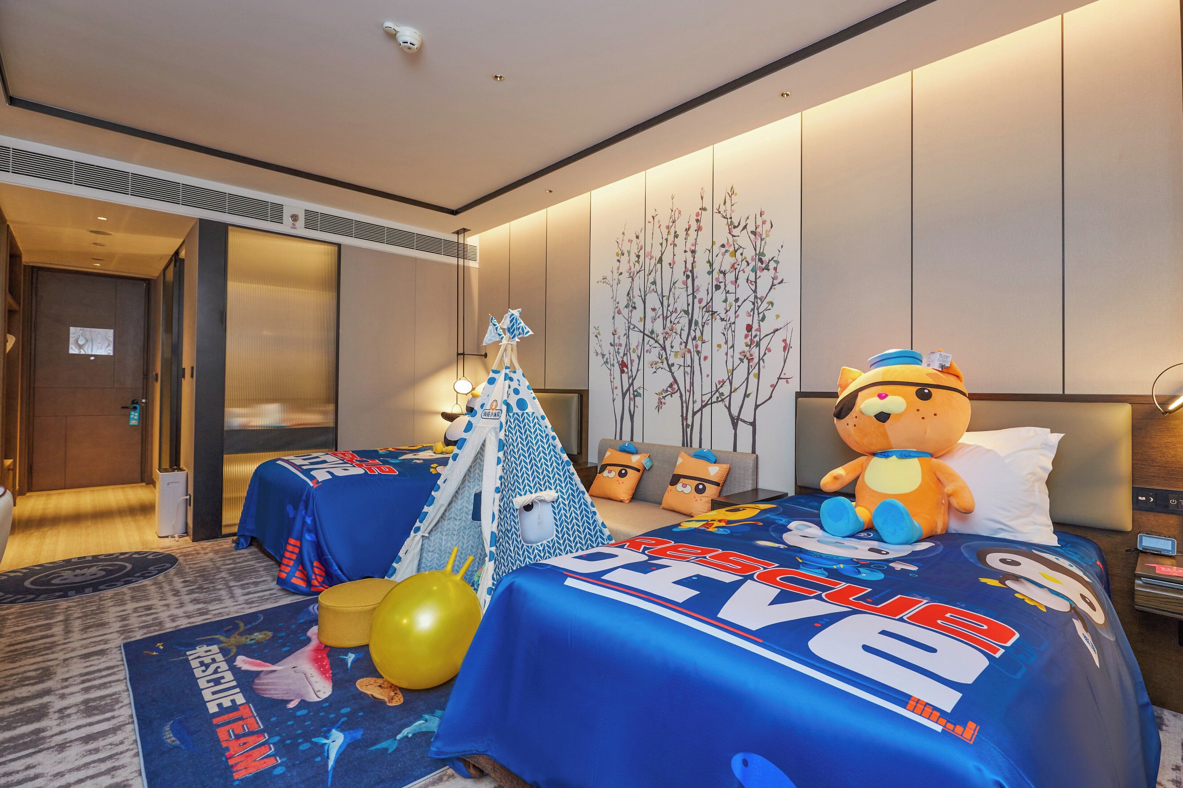 A hotel room with a bed featuring a 'Rescue Team' themed bedspread, a teddy bear, and a small tent-like structure.