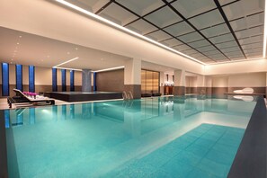 A large indoor swimming pool with a modern design, including a seating area with loungers and a small poolside bar. - Crowne Plaza Wuzhen by IHG (Jiaxing)