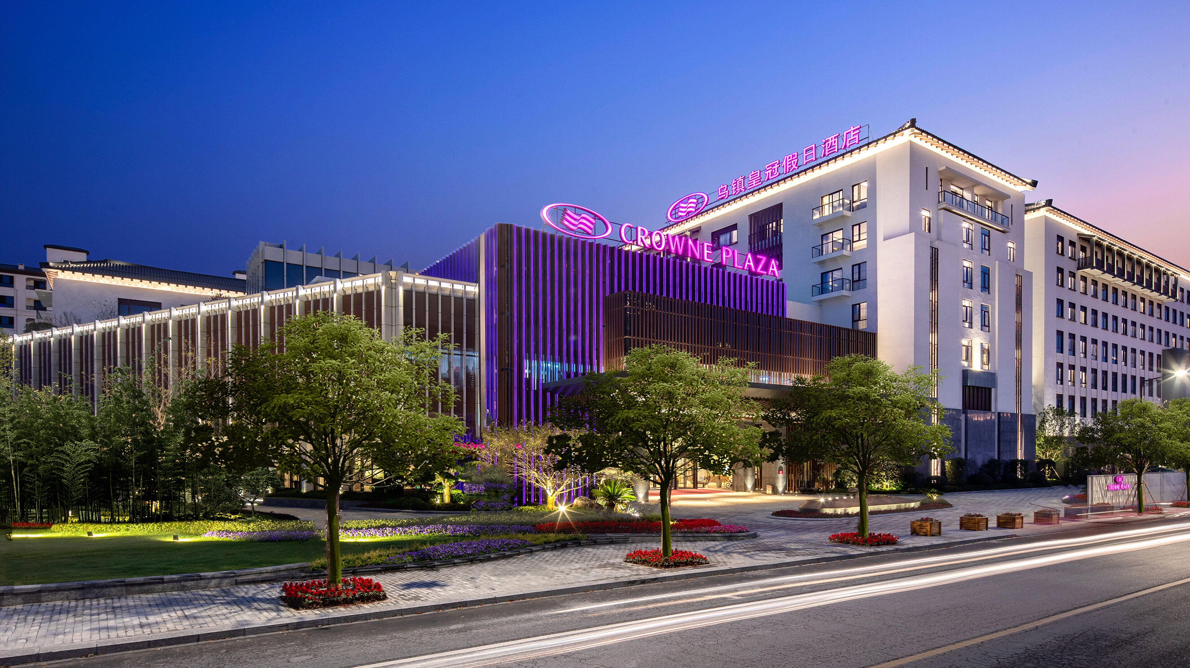 A hotel with a modern facade, a prominent neon sign, and a landscaped entrance area.