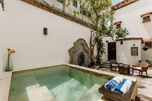 A pool area with a clear water surface, a stone wall with a decorative arch, and a seating area with wicker chairs and a table. - Casa Granada 24 (Cancun)