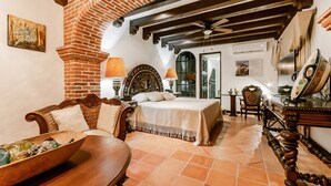 A bedroom with a bed, a wooden chair, a table, and a decorative mirror. - Casa Granada 24 (Cancun)