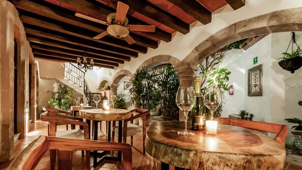 A cozy restaurant with wooden tables and benches, a ceiling fan, and potted plants. - Casa Granada 24 (Cancun)