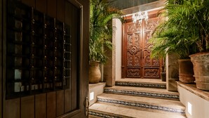 A set of ornate wooden doors with intricate carvings, flanked by large potted plants and leading up to a tiled staircase. - Casa Granada 24 (Cancun)