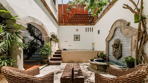 A courtyard with a wooden bench, wicker chairs, a fountain, and a staircase leading to an upper level. - Casa Granada 24 (Cancun)