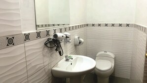 A bathroom with a white sink, a toilet, and a hairdryer on a wall-mounted stand.