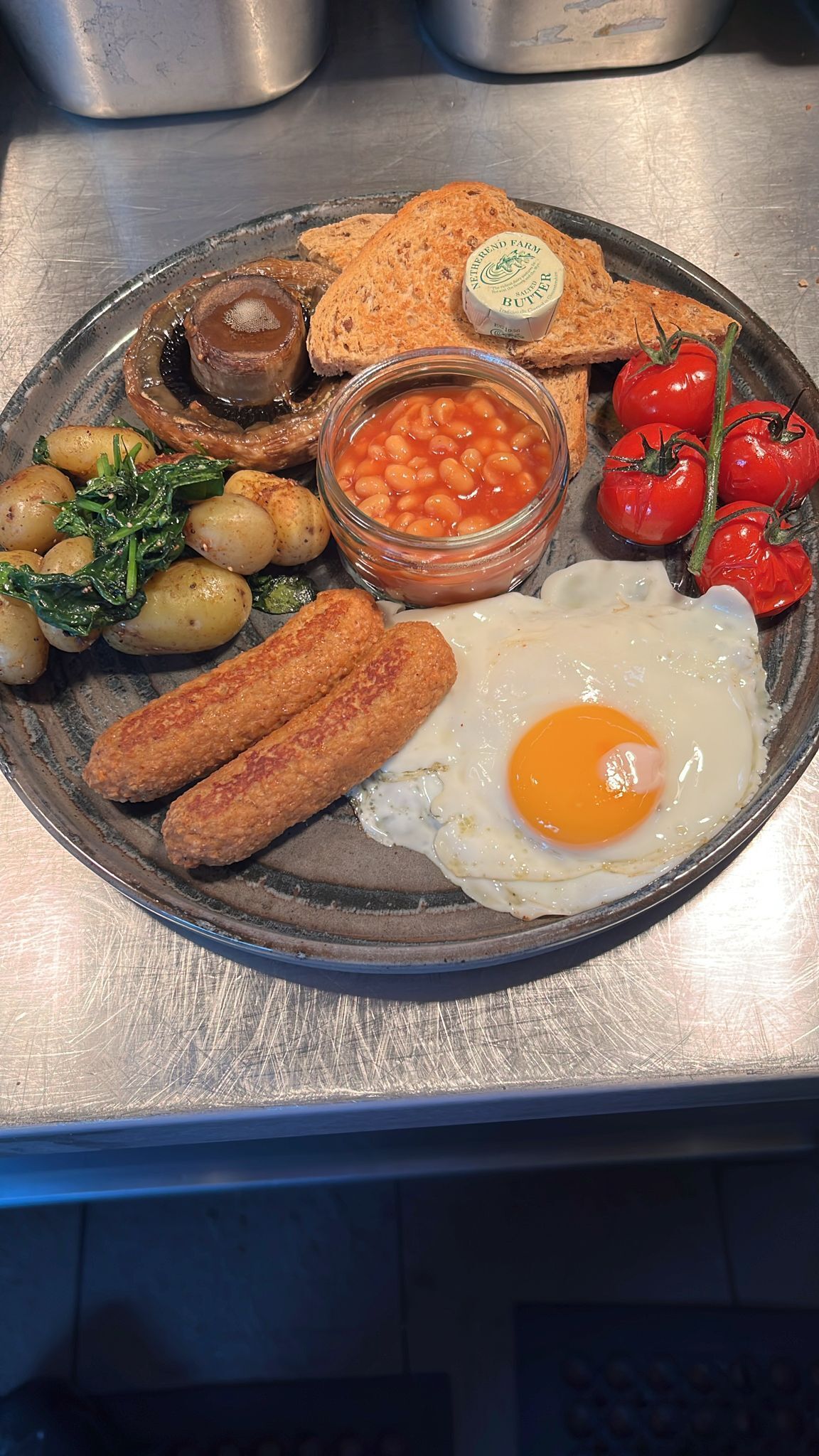 Un plato de desayuno con tostadas, frijoles, tomates, huevos, salchichas y champiñones.