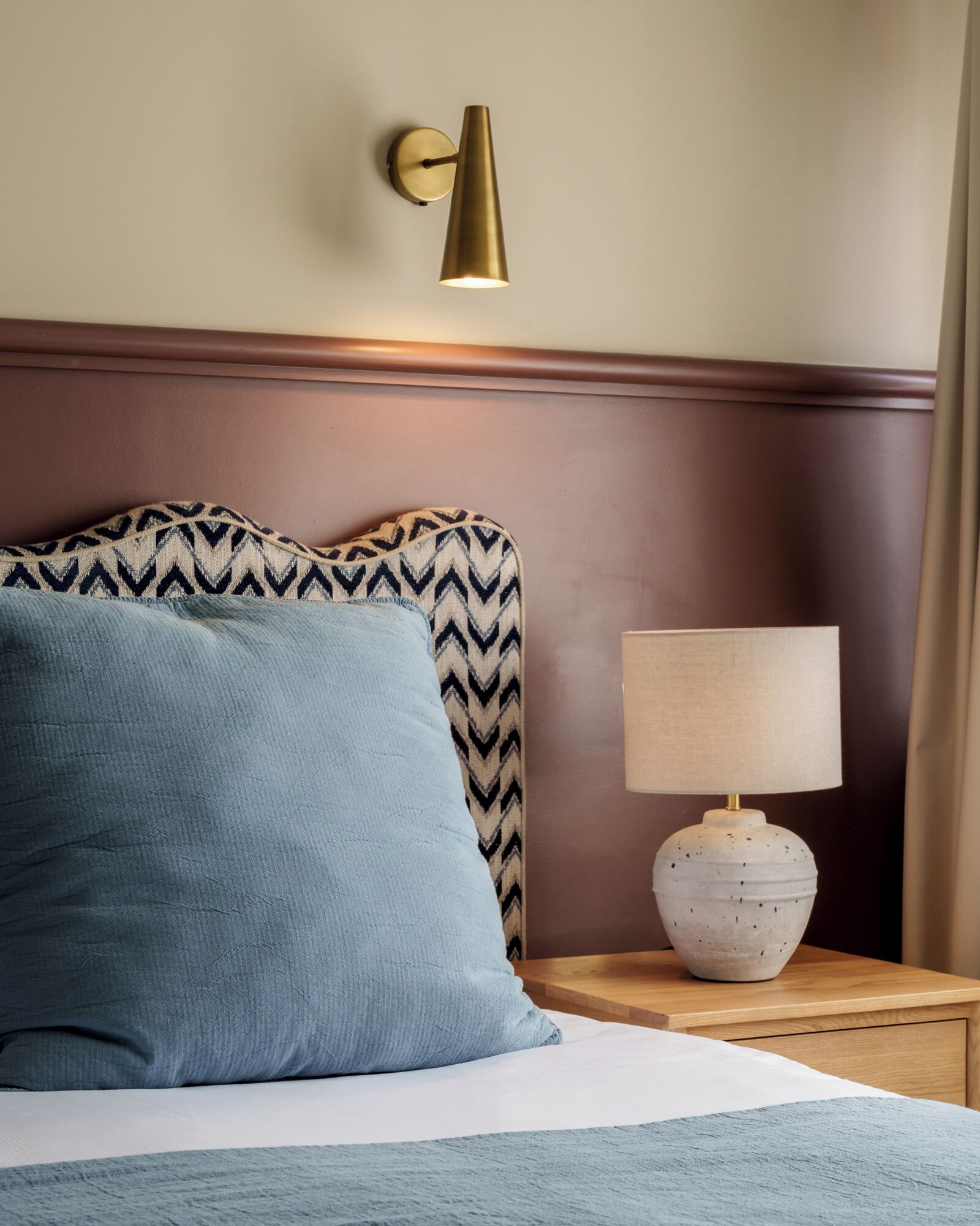 Una cama con almohadas estampadas, una lámpara de pared y una mesita de noche con lámpara.