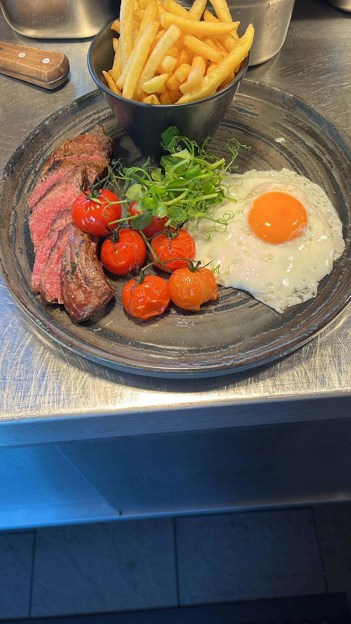 A plate with steak, cherry tomatoes, greens, and a fried egg.