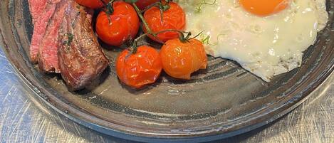 A plate with steak, cherry tomatoes, greens, and a fried egg.
