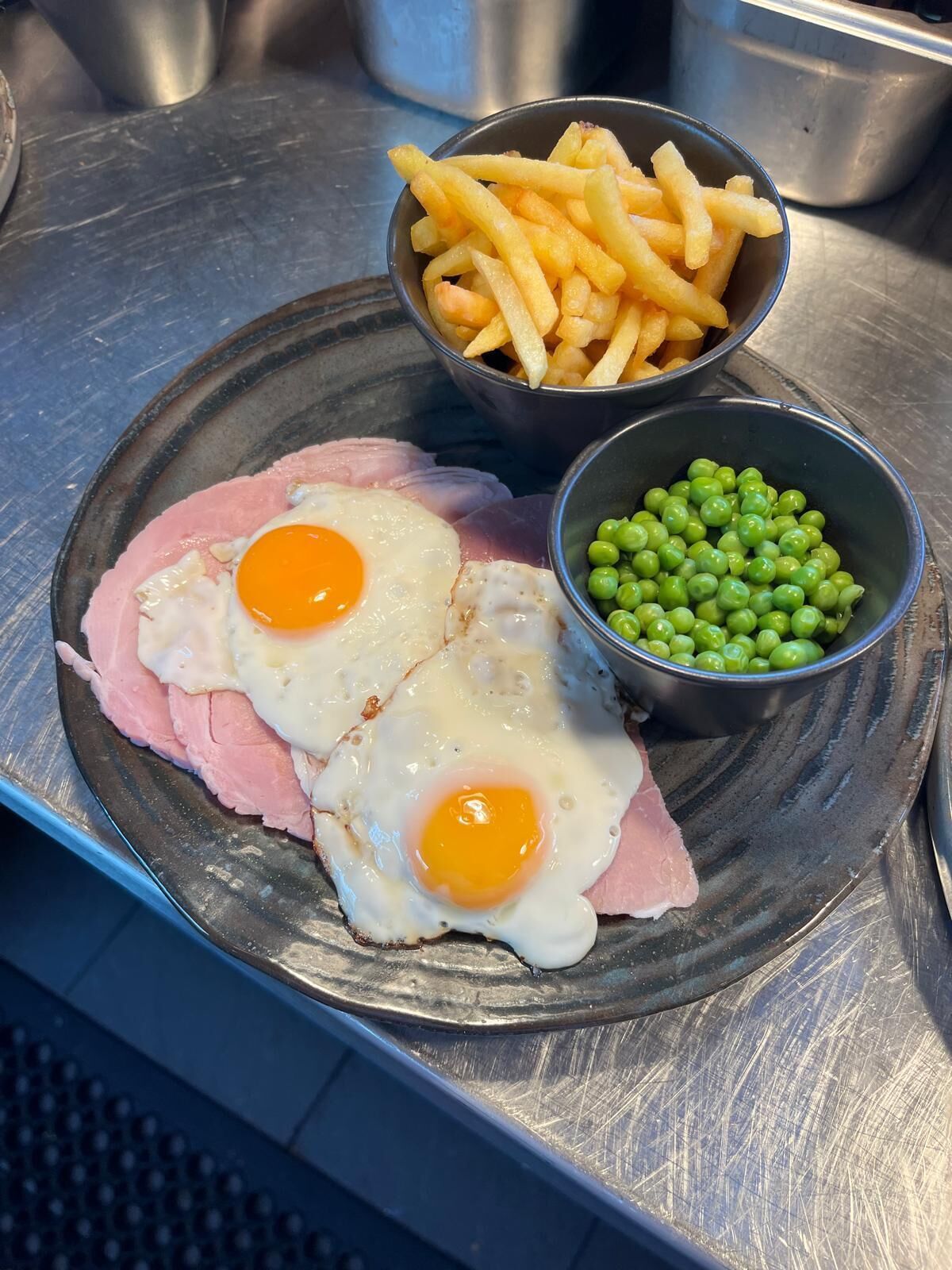 Un plato con jamón, dos huevos fritos, papas fritas y guisantes.