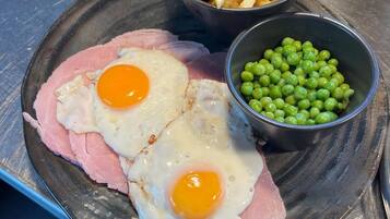 A plate with ham, two fried eggs, French fries, and peas.