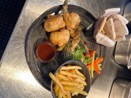 En tallerken med friturestegt mad, en lille skål sauce, pommes frites og grøntsager.