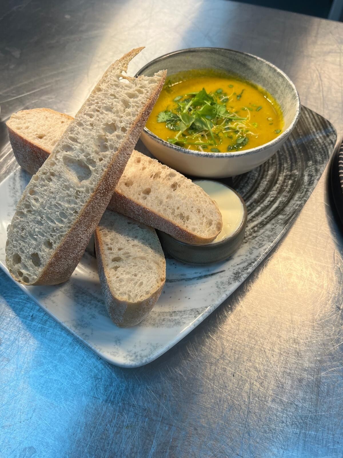 Un plato con rebanadas de pan y un tazón de sopa sobre una mesa con textura.