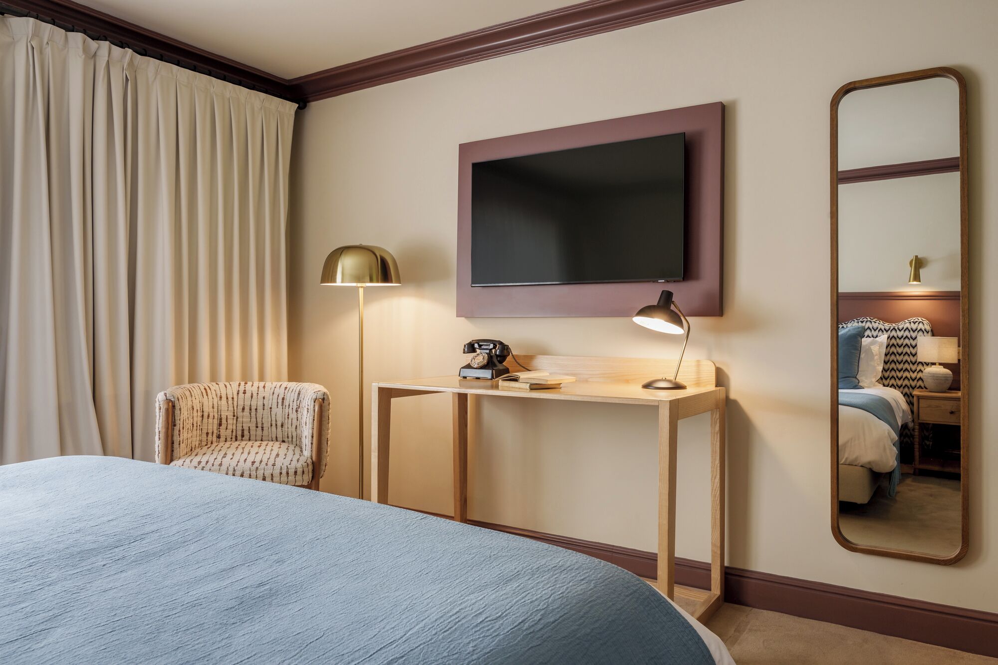 A hotel room with a bed, a desk with a lamp, a chair, a flat-screen TV, and a mirror.