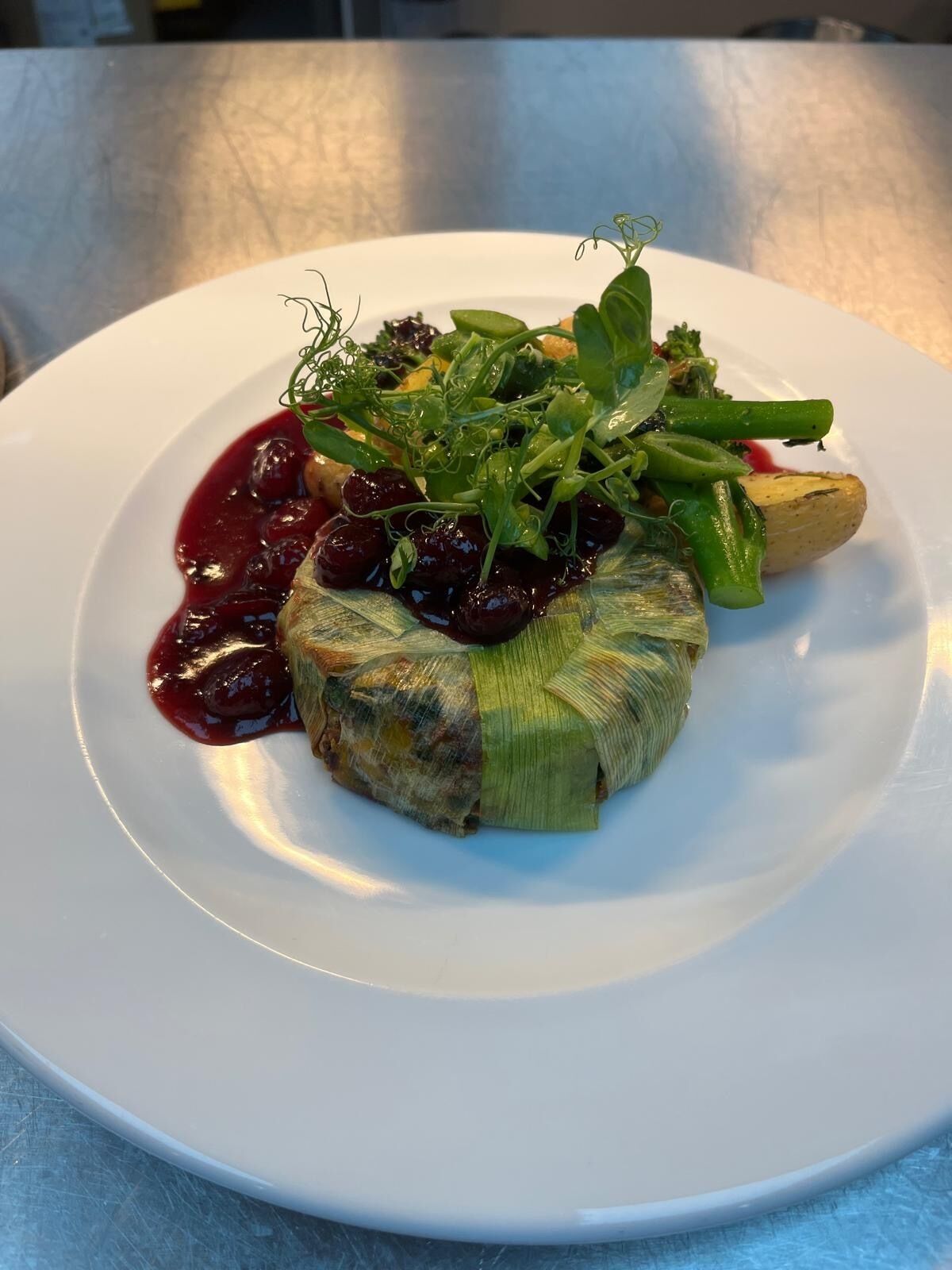 A white plate with a dish consisting of a wrapped item, possibly a vegetable or meat, garnished with greens and a red sauce.