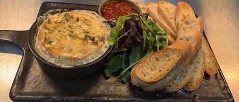 A dish of baked fish with a side of greens and bread on a black plate.