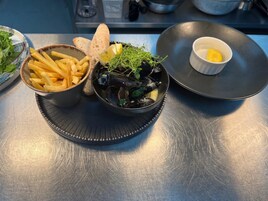 Un plato de mejillones, papas fritas y pan sobre una mesa de metal.