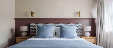 Una cama bien hecha con un edredón azul y dos almohadas, flanqueada por mesitas de noche con lámparas, en una habitación de diseño sencillo y limpio.