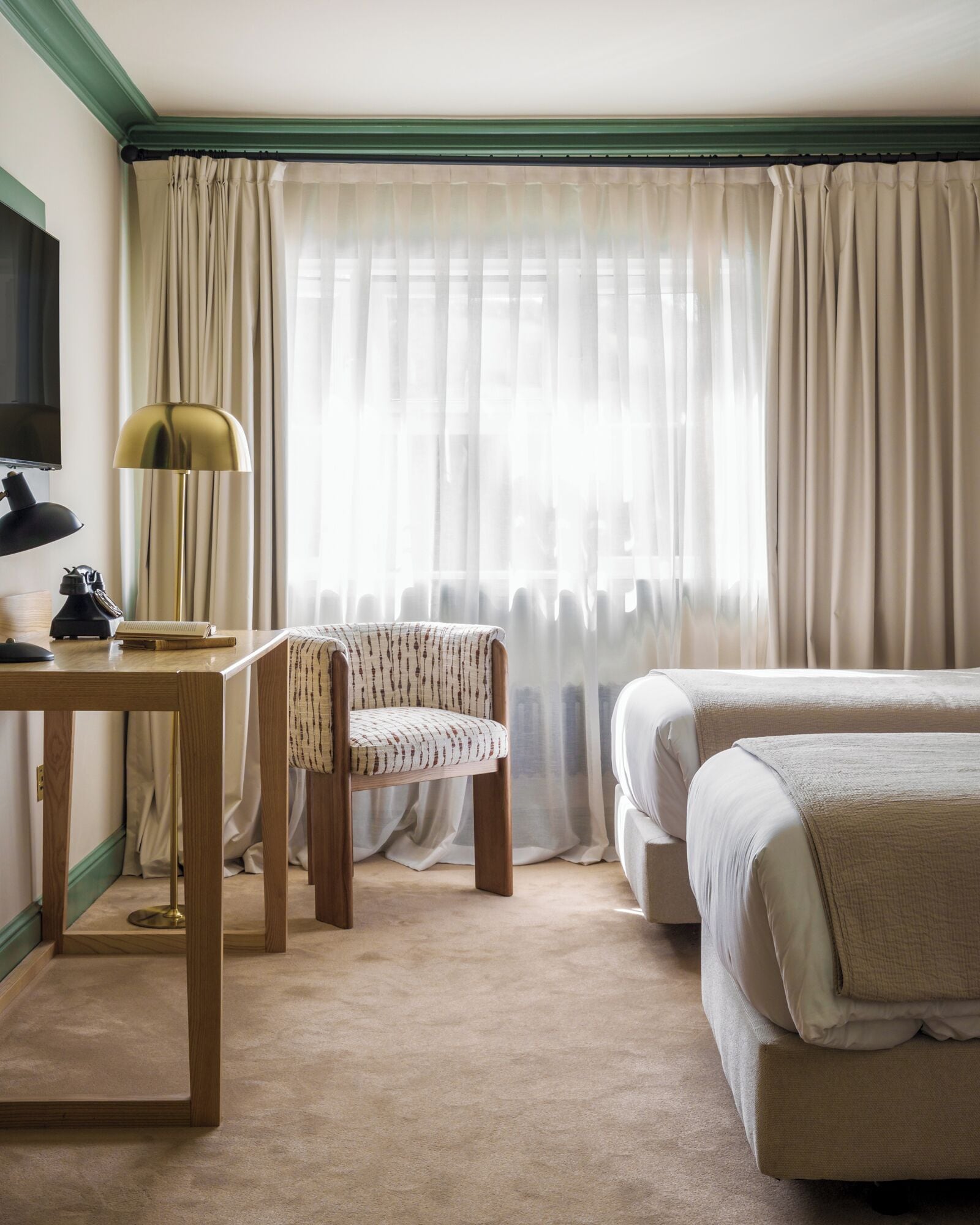 A hotel room with a wooden desk, a chair, a bed, and a large window with curtains.
